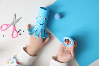 Photo of Little girl with handmade octopus at white table, top view. Child creativity and craft