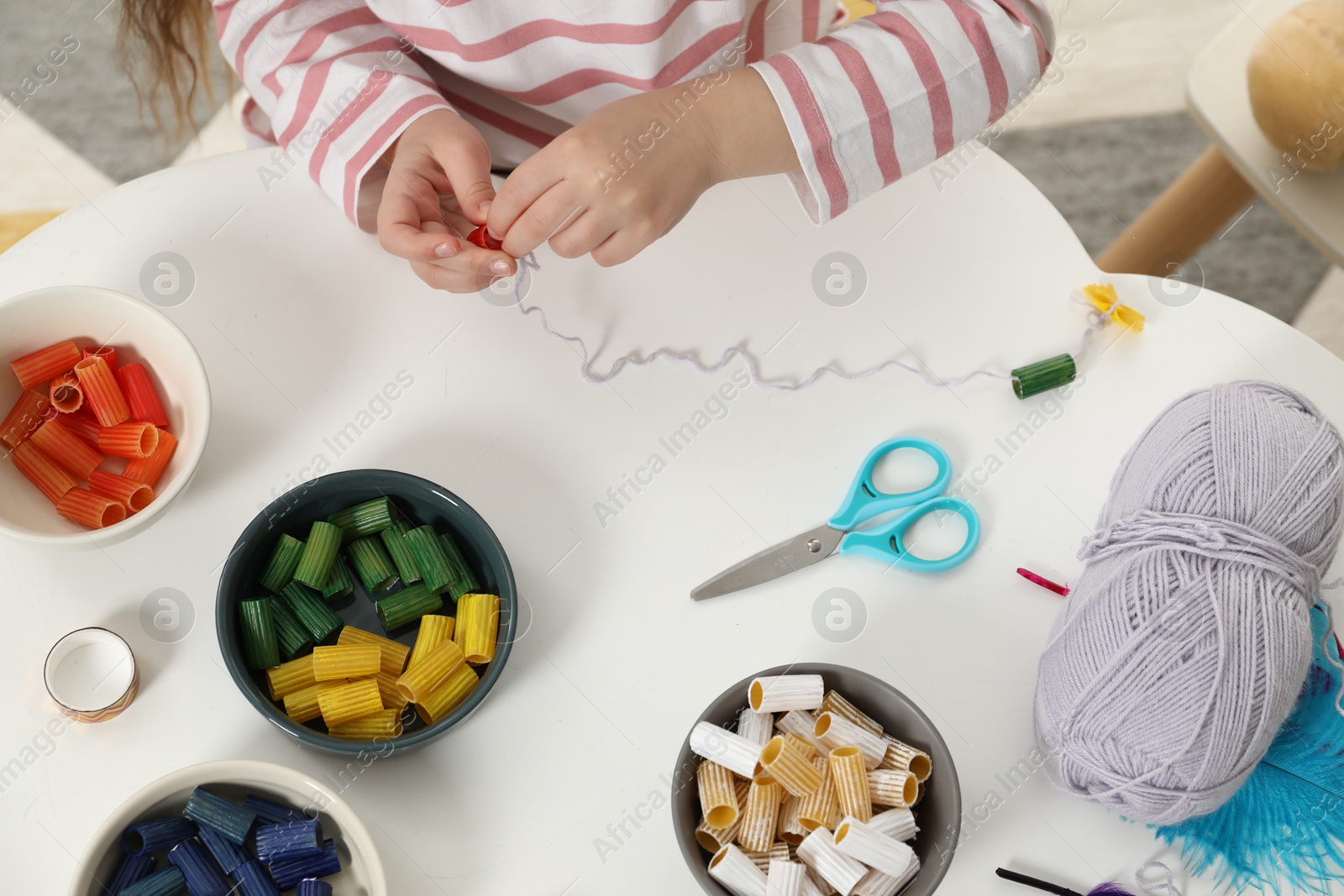 Photo of Little girl making craft at white table indoors, top view. Child creativity and handmade handicraft