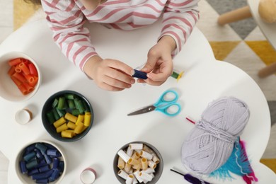 Photo of Little girl making craft at white table indoors, top view. Child creativity and handmade handicraft