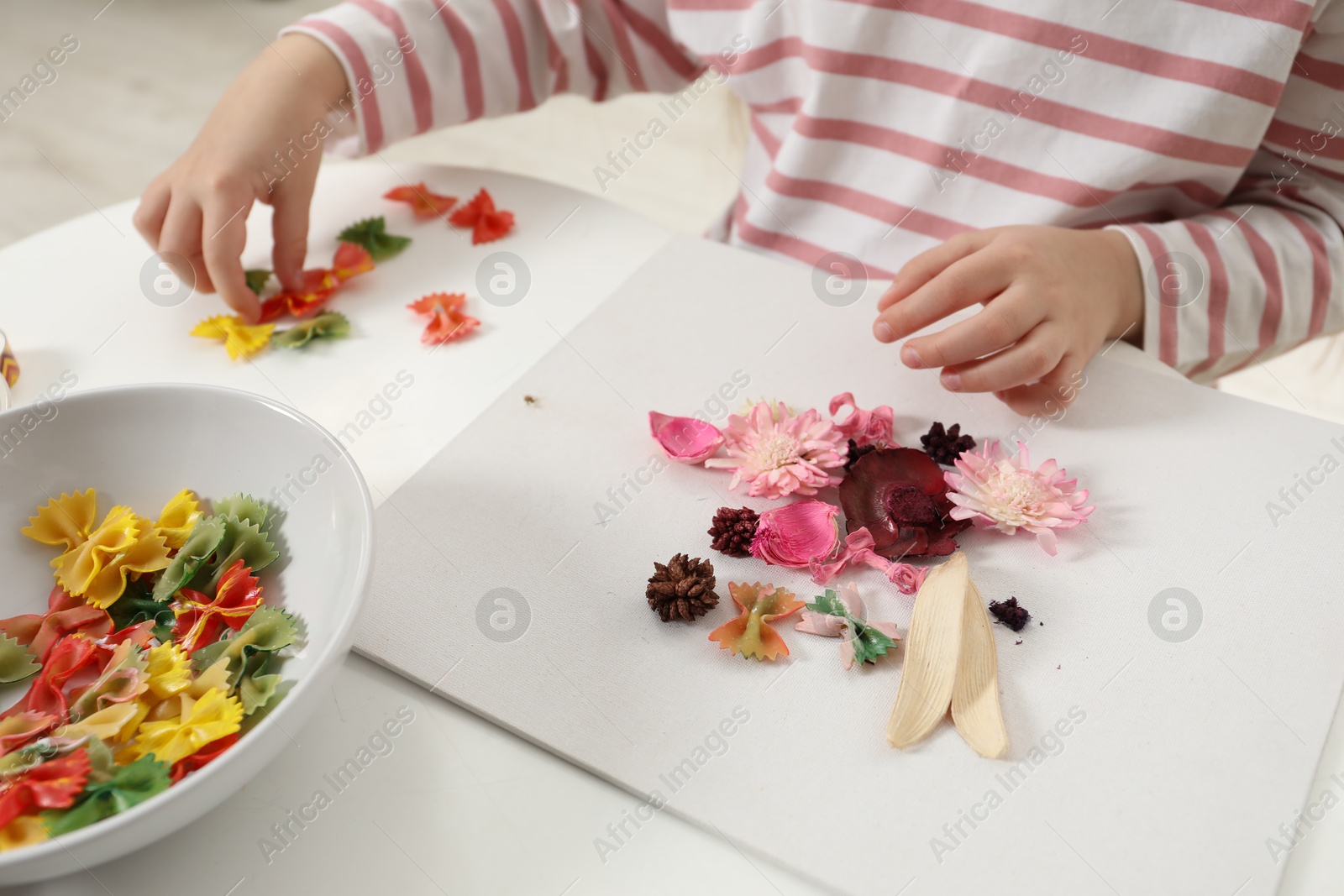 Photo of Little girl making craft at white table indoors, closeup. Child creativity and handmade handicraft