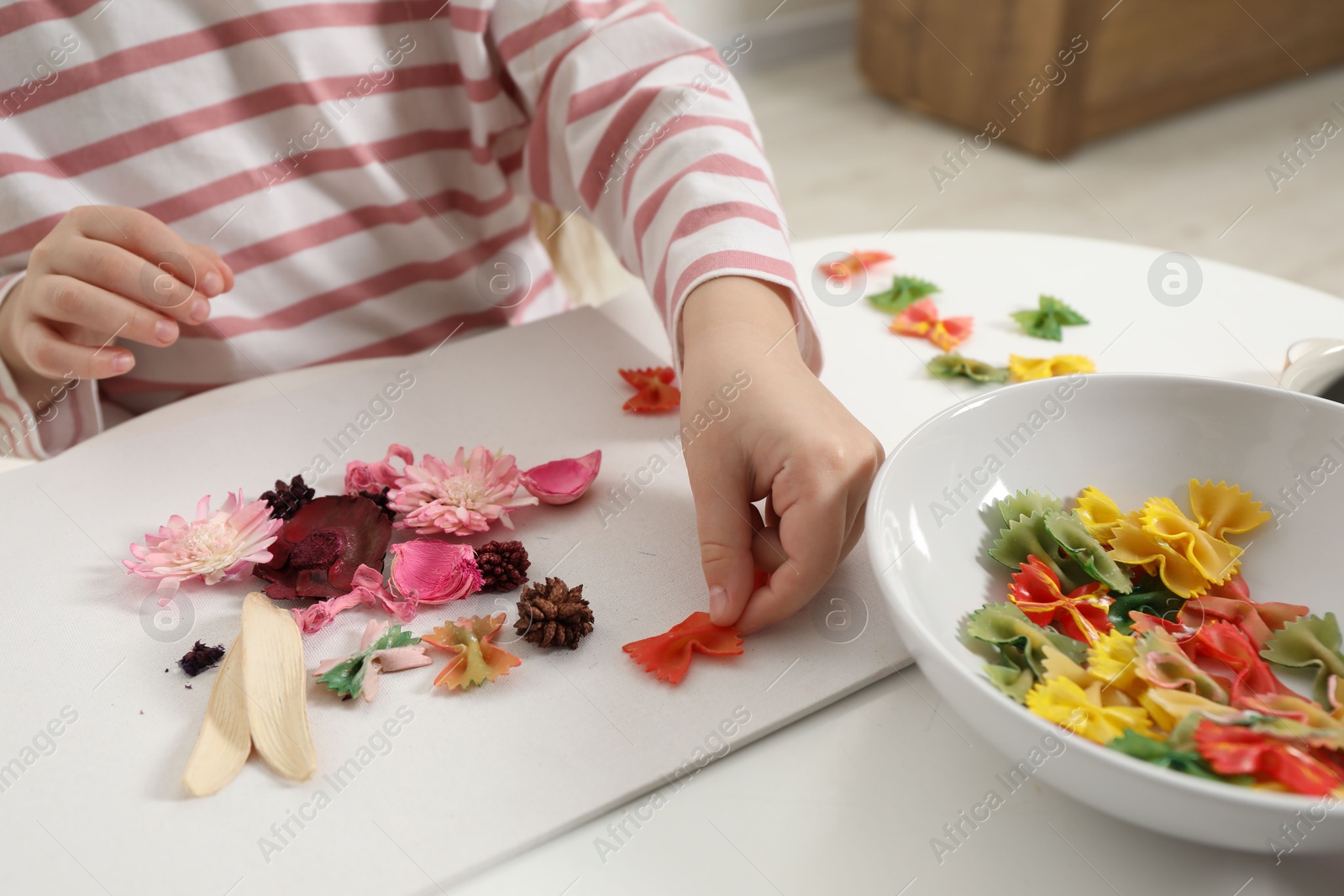 Photo of Little girl making craft at white table indoors, closeup. Child creativity and handmade handicraft