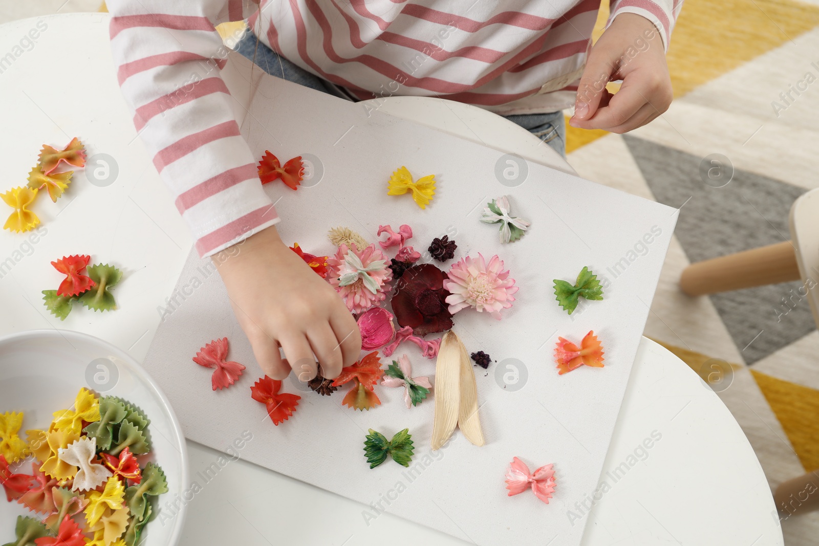 Photo of Little girl making craft at white table indoors, top view. Child creativity and handmade handicraft