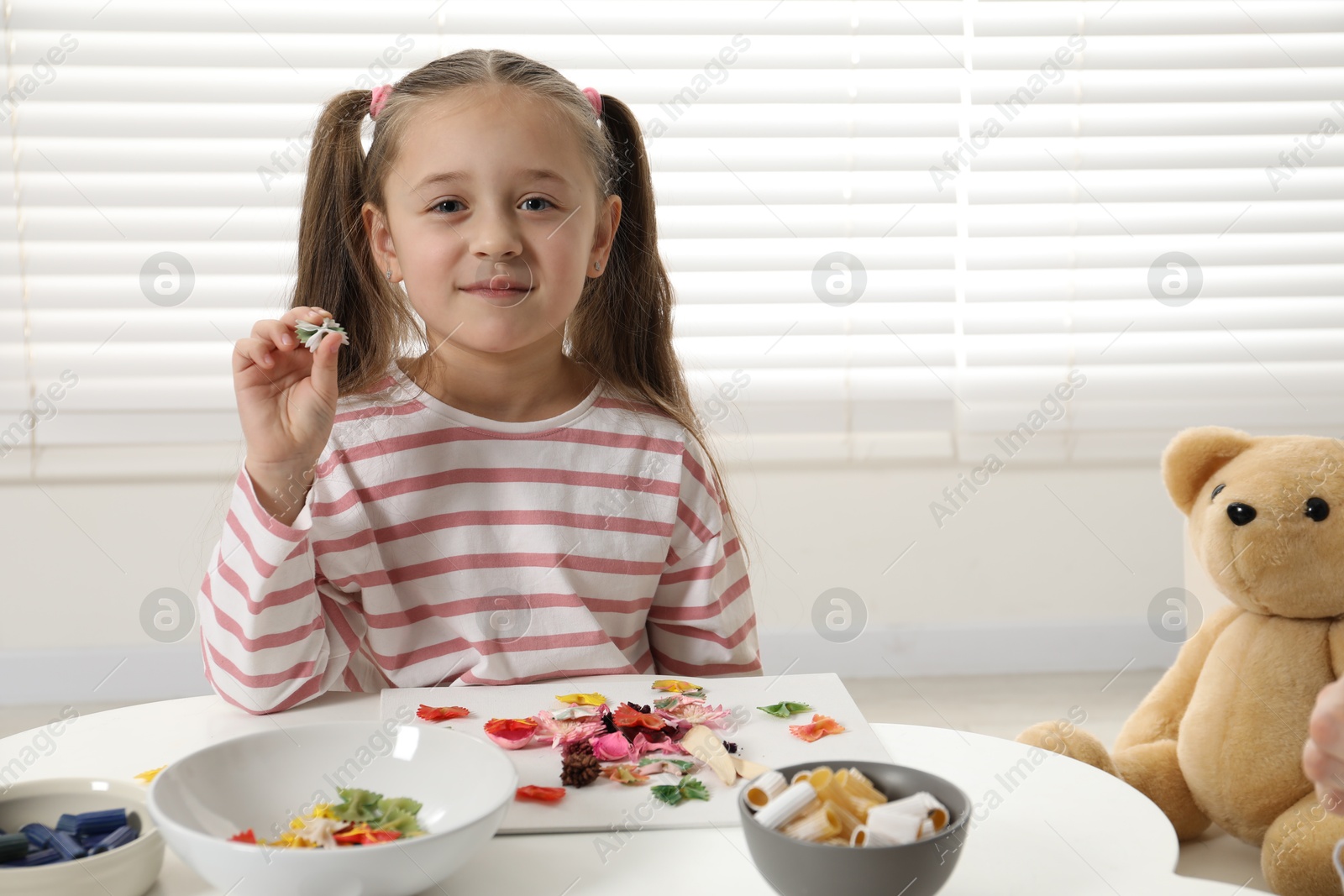 Photo of Little girl making craft at white table indoors. Child creativity and handmade handicraft