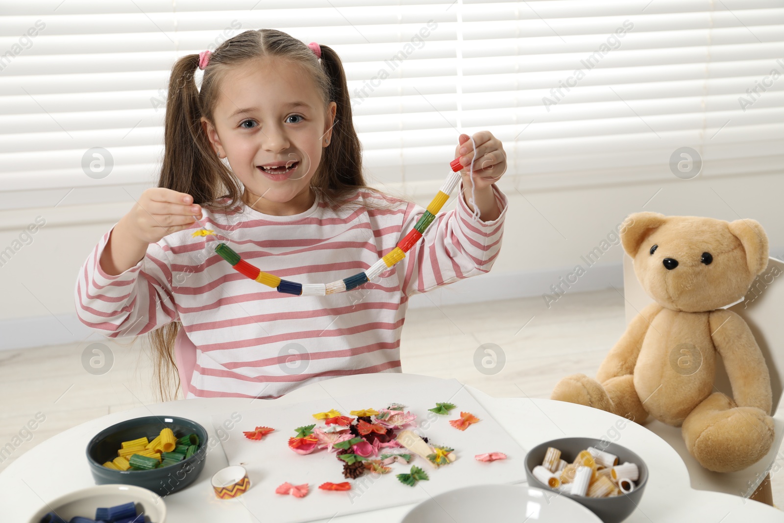 Photo of Little girl with handmade necklace at home. Child creativity and craft