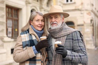 Photo of Family portrait of happy elderly couple with paper cups on city street