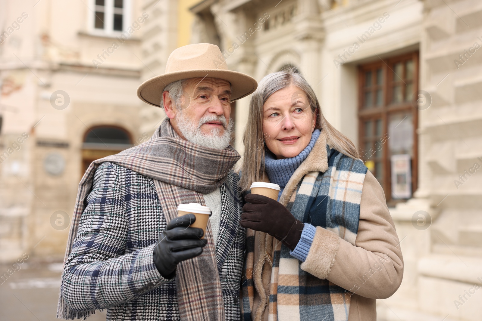 Photo of Family portrait of happy elderly couple with paper cups on city street