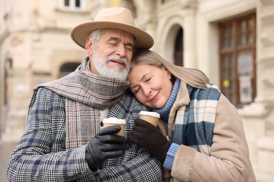 Photo of Family portrait of happy elderly couple with paper cups on city street