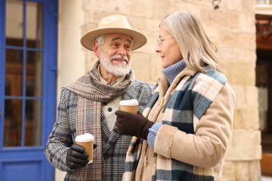 Photo of Happy elderly couple with coffee cups walking on city street