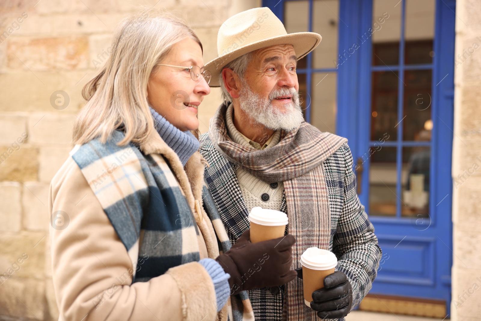 Photo of Happy elderly couple with coffee cups walking on city street