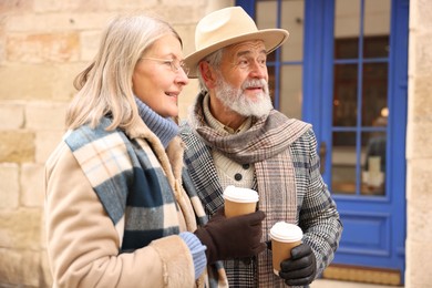 Photo of Happy elderly couple with coffee cups walking on city street