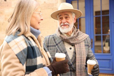 Photo of Happy elderly couple with coffee cups walking on city street