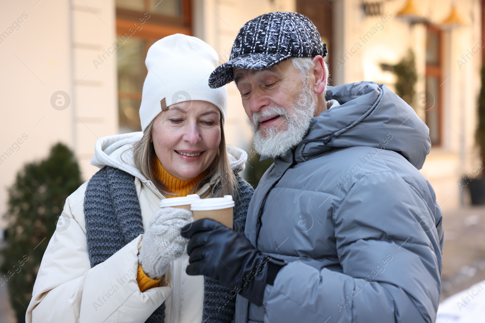 Photo of Happy elderly couple with paper cups on city street