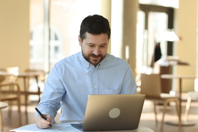 Photo of Handsome business owner working with laptop at table in his cafe