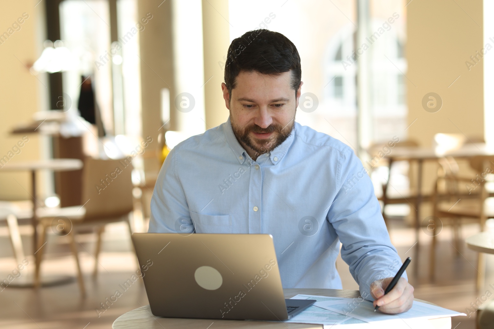 Photo of Handsome business owner working with laptop at table in his cafe