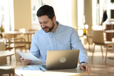 Photo of Handsome business owner working with laptop at table in his cafe