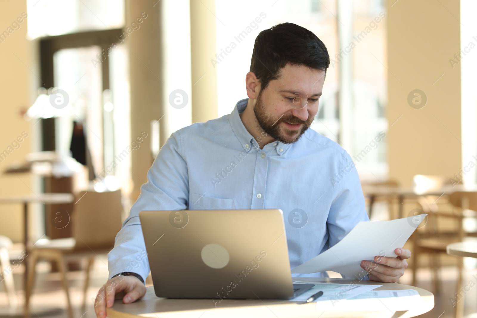 Photo of Handsome business owner working with laptop at table in his cafe