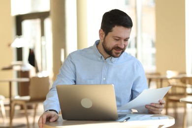 Photo of Handsome business owner working with laptop at table in his cafe