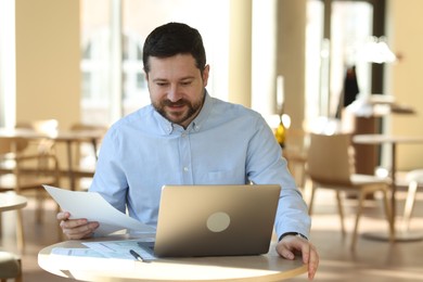 Photo of Handsome business owner working with laptop at table in his cafe