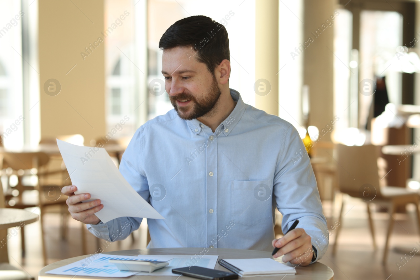 Photo of Smiling business owner doing paperwork at table in his cafe