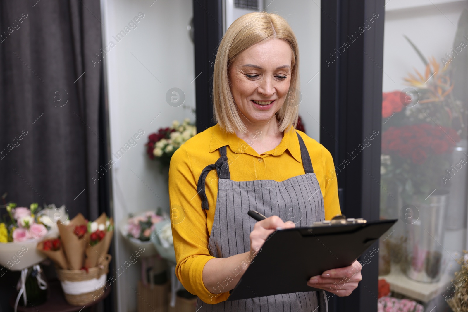 Photo of Business owner with clipboard taking notes in her flower shop, space for text