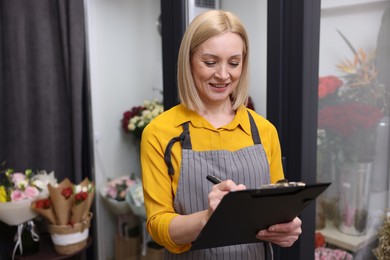 Photo of Business owner with clipboard taking notes in her flower shop, space for text