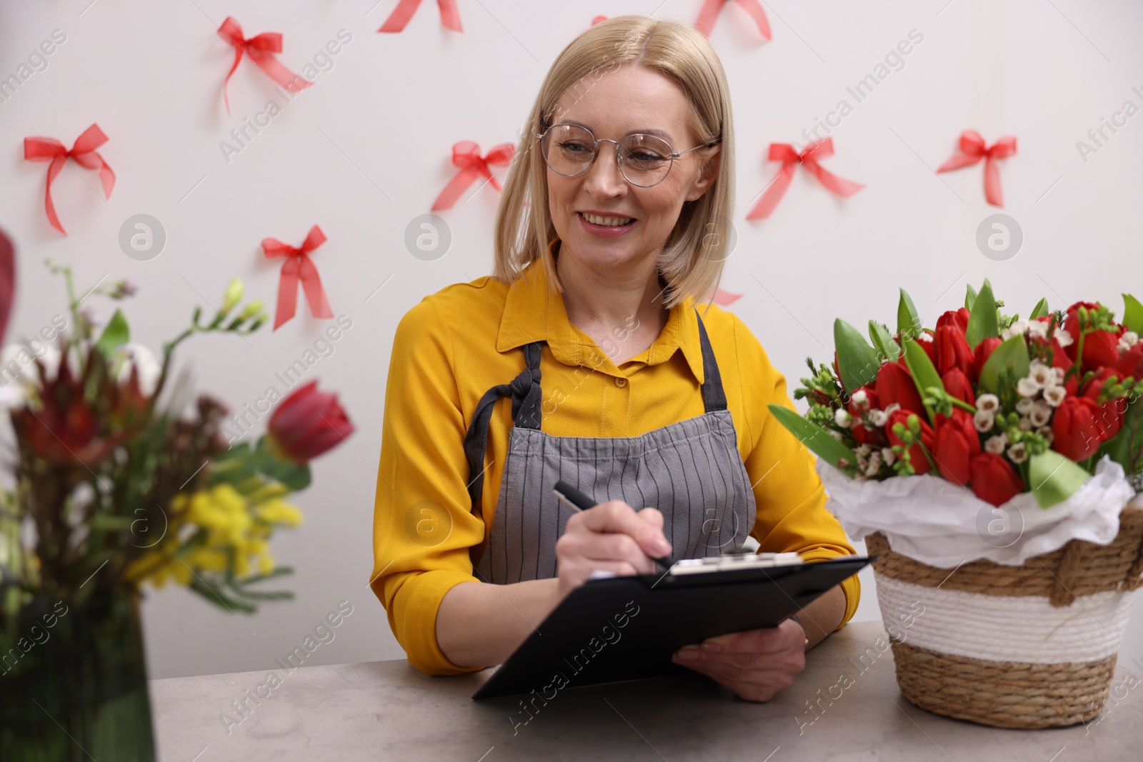 Photo of Business owner with clipboard taking notes at table in her flower shop