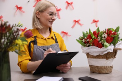 Photo of Business owner with clipboard taking notes at table in her flower shop