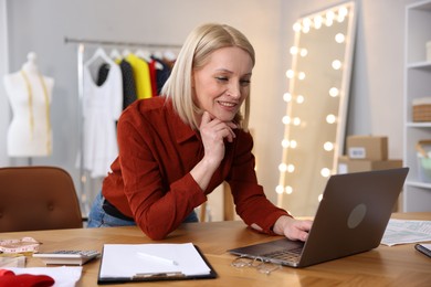 Photo of Business owner working on laptop at table in her tailor shop