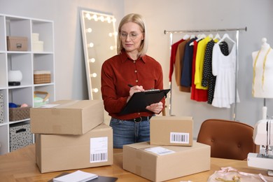 Photo of Business owner taking notes near table with parcels in her tailor shop