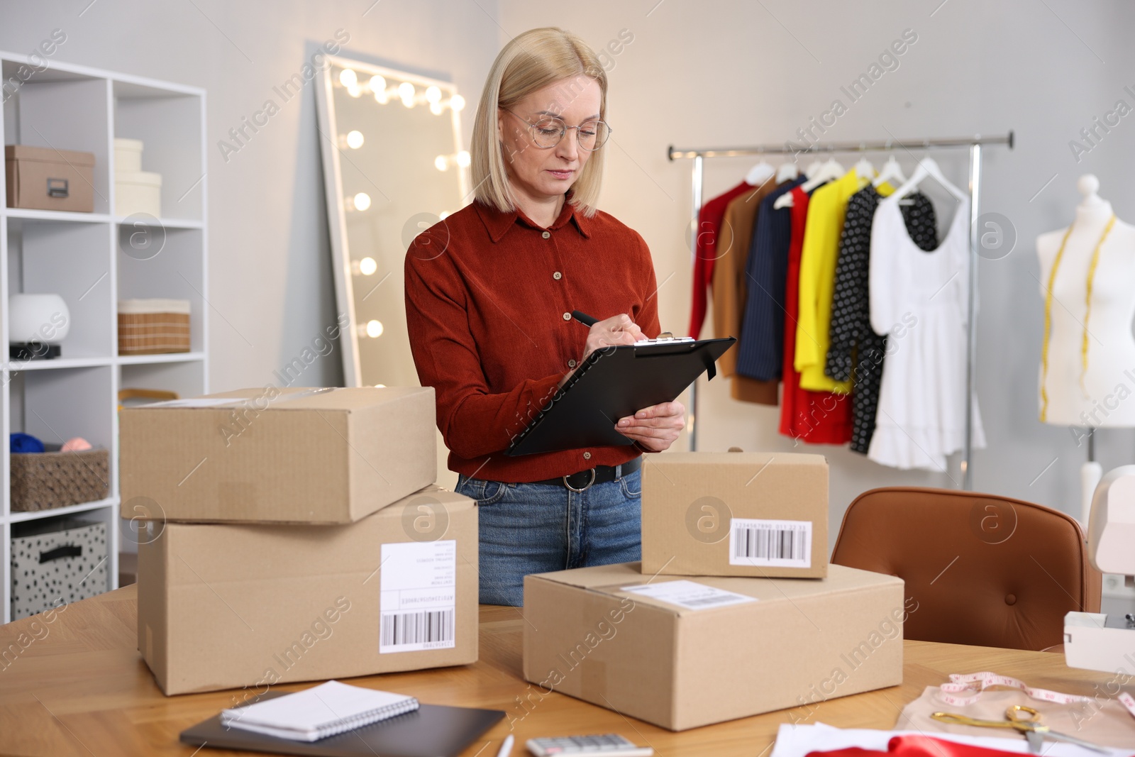 Photo of Business owner taking notes near table with parcels in her tailor shop