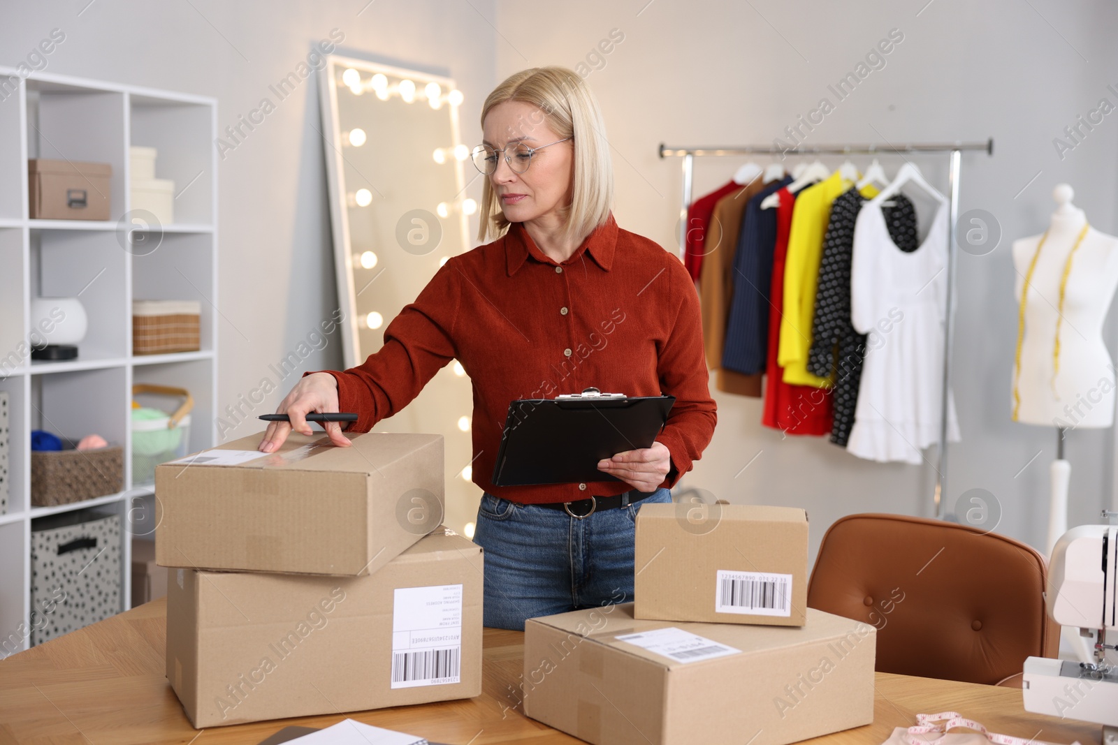 Photo of Business owner taking notes near table with parcels in her tailor shop