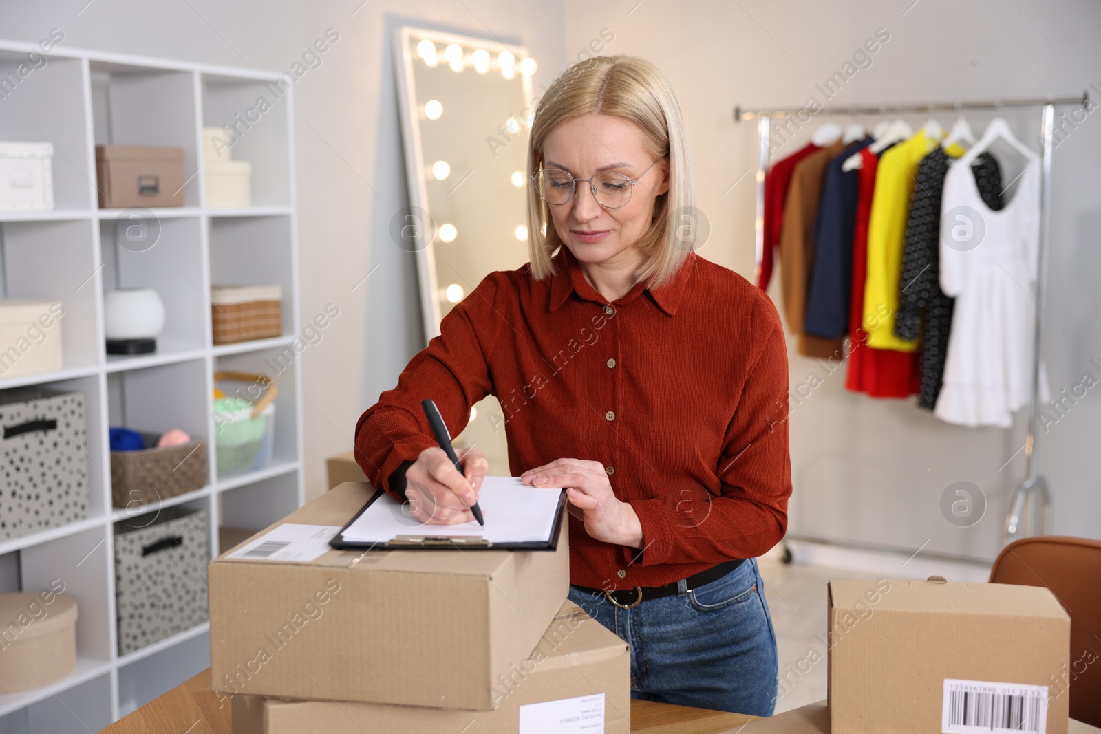 Photo of Business owner taking notes near parcels in her tailor shop