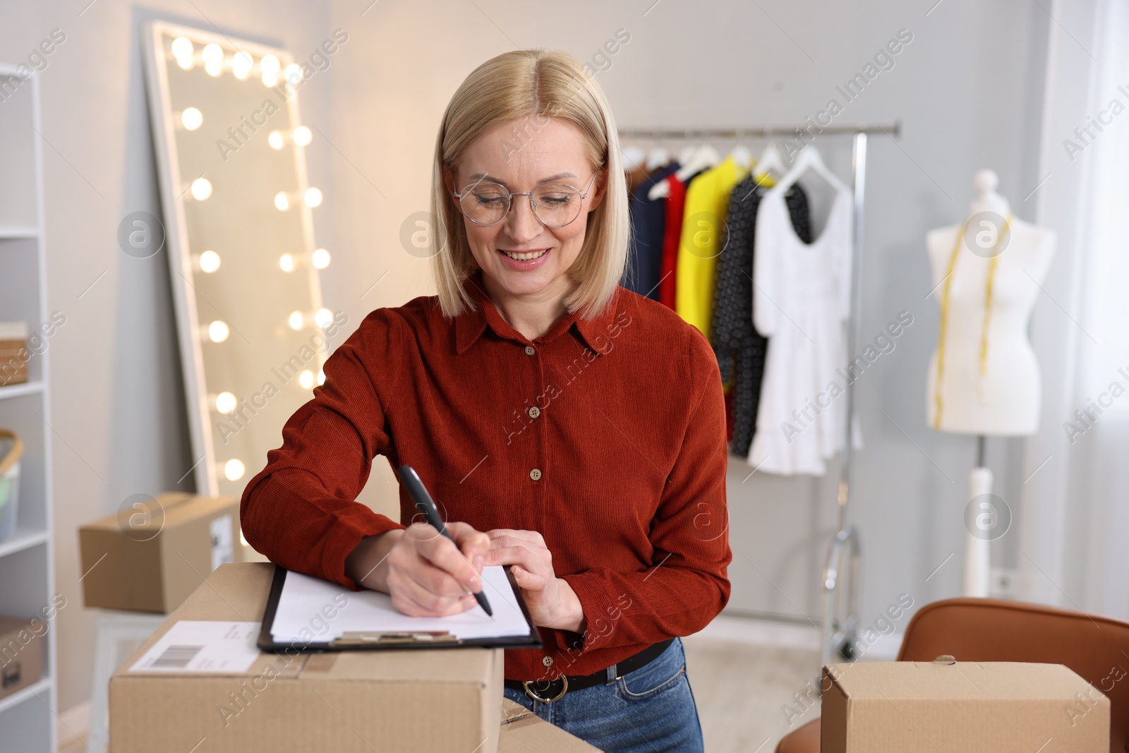 Photo of Business owner taking notes near parcels in her tailor shop