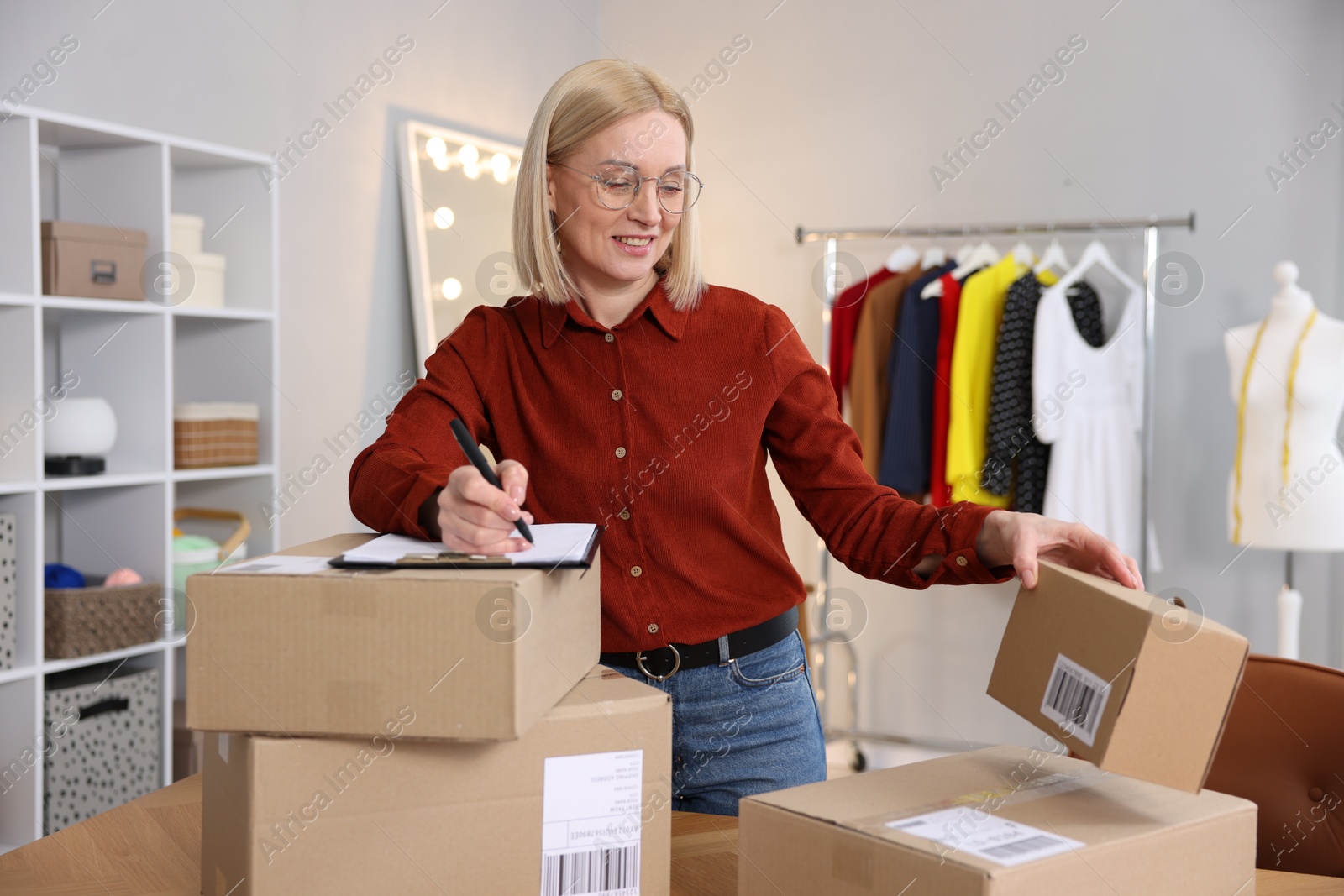 Photo of Business owner taking notes near parcels in her tailor shop