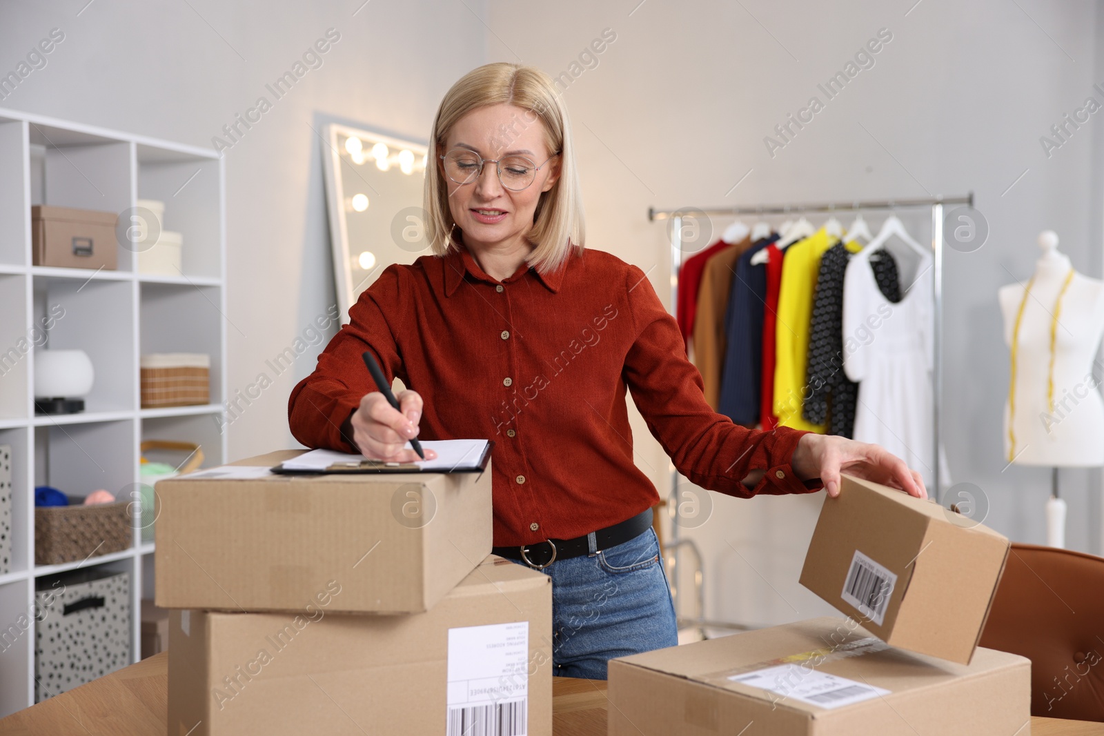 Photo of Business owner taking notes near parcels in her tailor shop