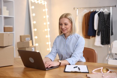 Photo of Business owner working on laptop at table in her tailor shop