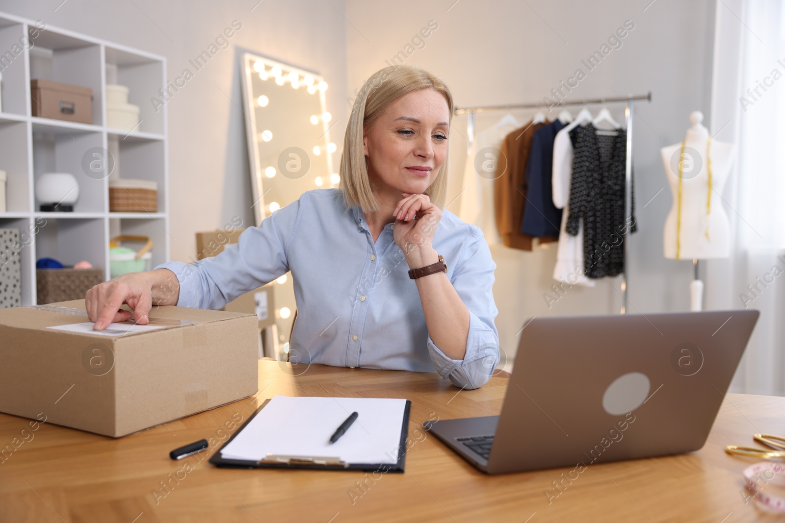 Photo of Business owner with parcel at table in her tailor shop