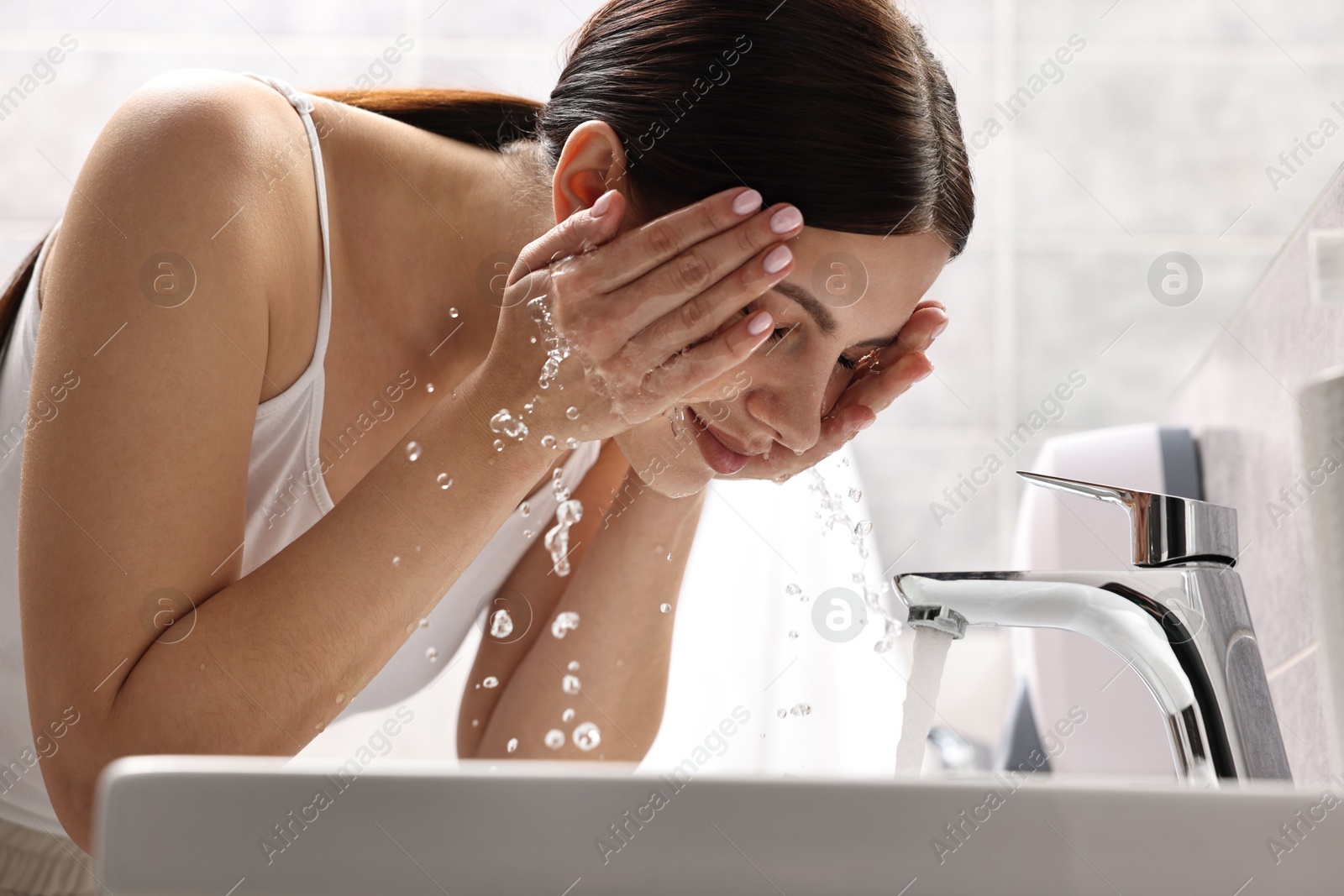 Photo of Woman washing her face over sink in bathroom