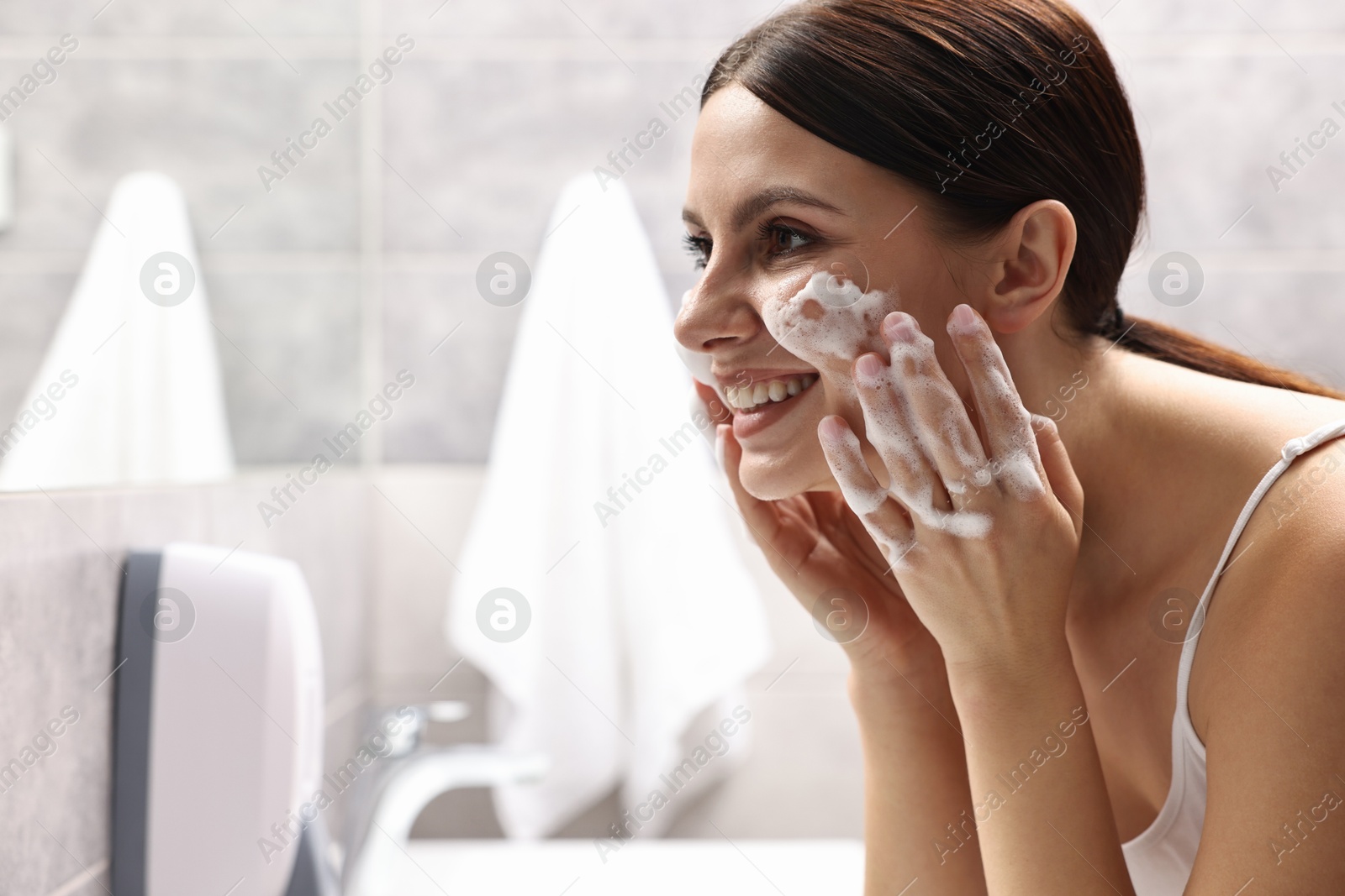 Photo of Woman washing her face with cleansing foam in bathroom, space for text