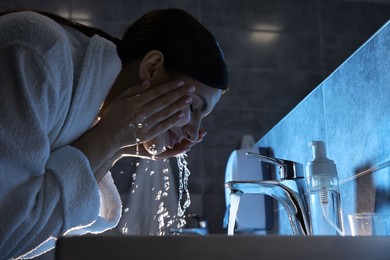 Photo of Woman washing her face over sink in bathroom