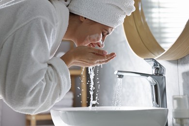 Photo of Woman washing her face over sink in bathroom