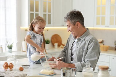 Photo of Father and his daughter making dough at white marble table in kitchen