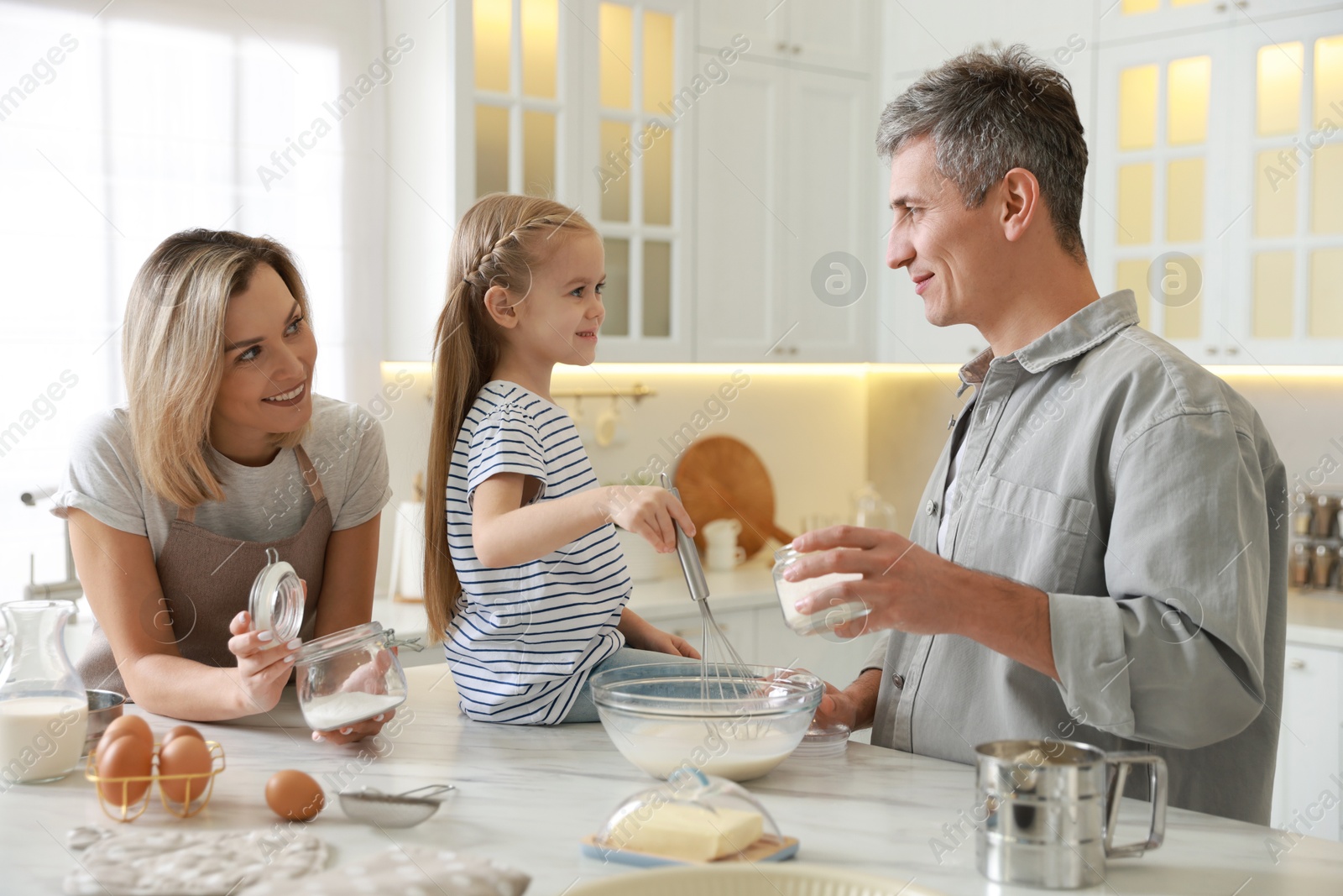 Photo of Happy parents and their daughter making dough at white marble table in kitchen