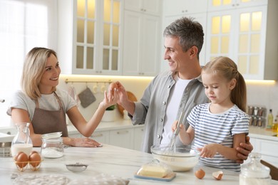 Photo of Happy parents and their daughter making dough at white marble table in kitchen