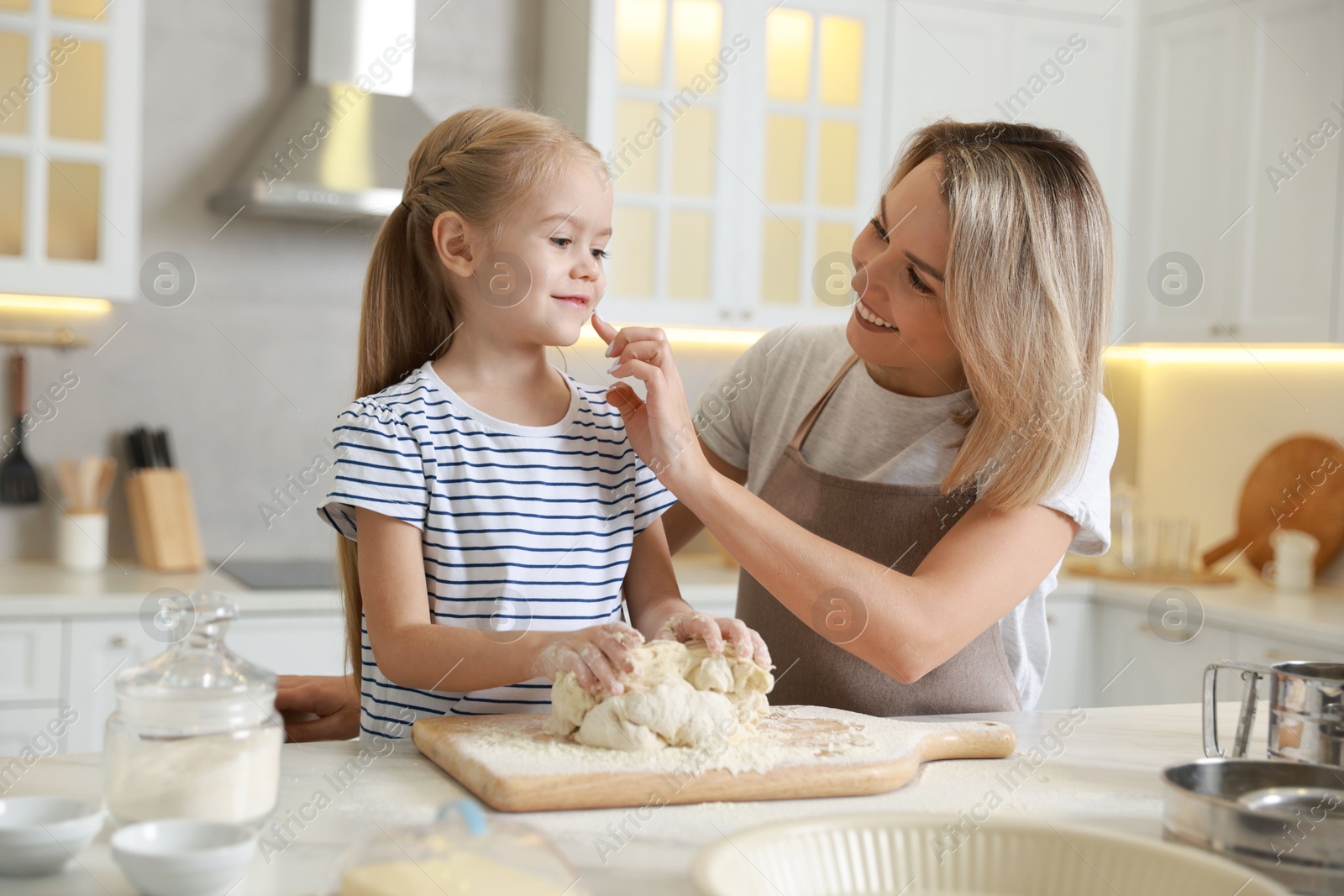 Photo of Mother and her daughter kneading dough at table in kitchen