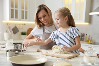 Photo of Mother and her daughter kneading dough at table in kitchen