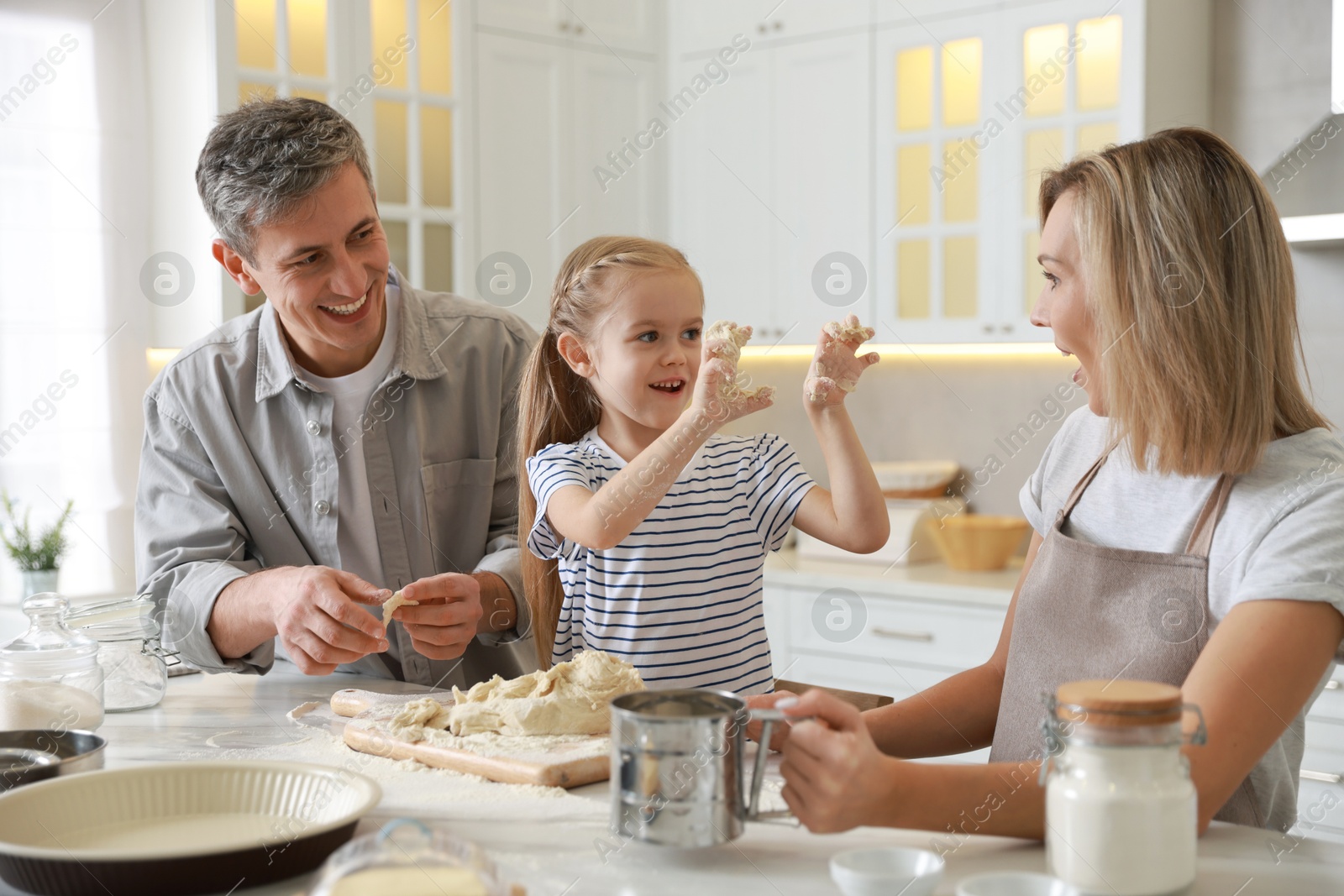 Photo of Happy parents and their daughter making dough at white marble table in kitchen