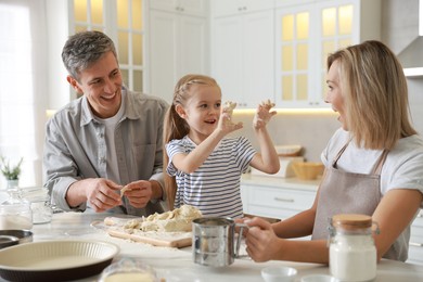 Photo of Happy parents and their daughter making dough at white marble table in kitchen