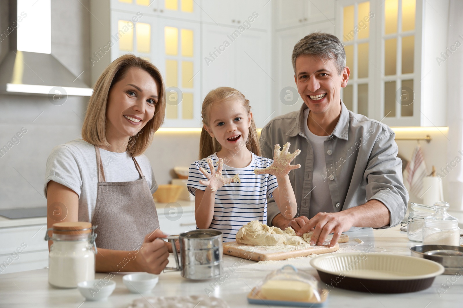 Photo of Happy parents and their daughter making dough at white marble table in kitchen