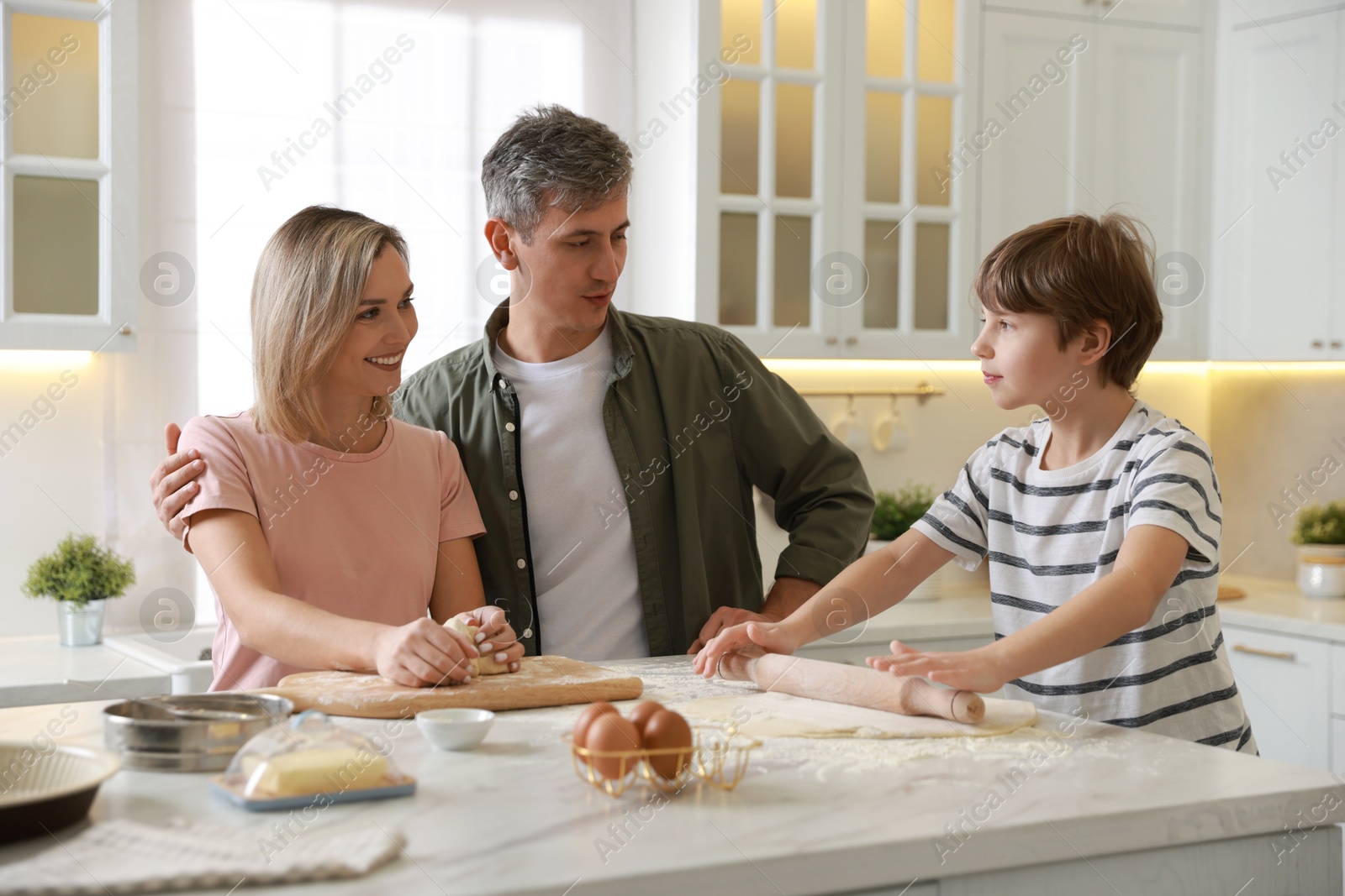 Photo of Happy family kneading dough at white marble table in kitchen